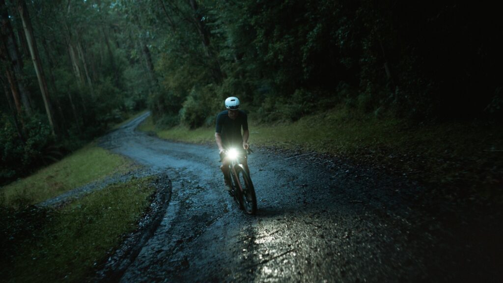 Rider with a headlight on a wet gravel road through forest at night