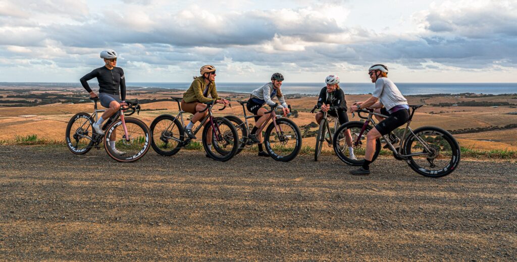 Five riders with Simpatico titanium gravel bikes on a gravel road above farmland