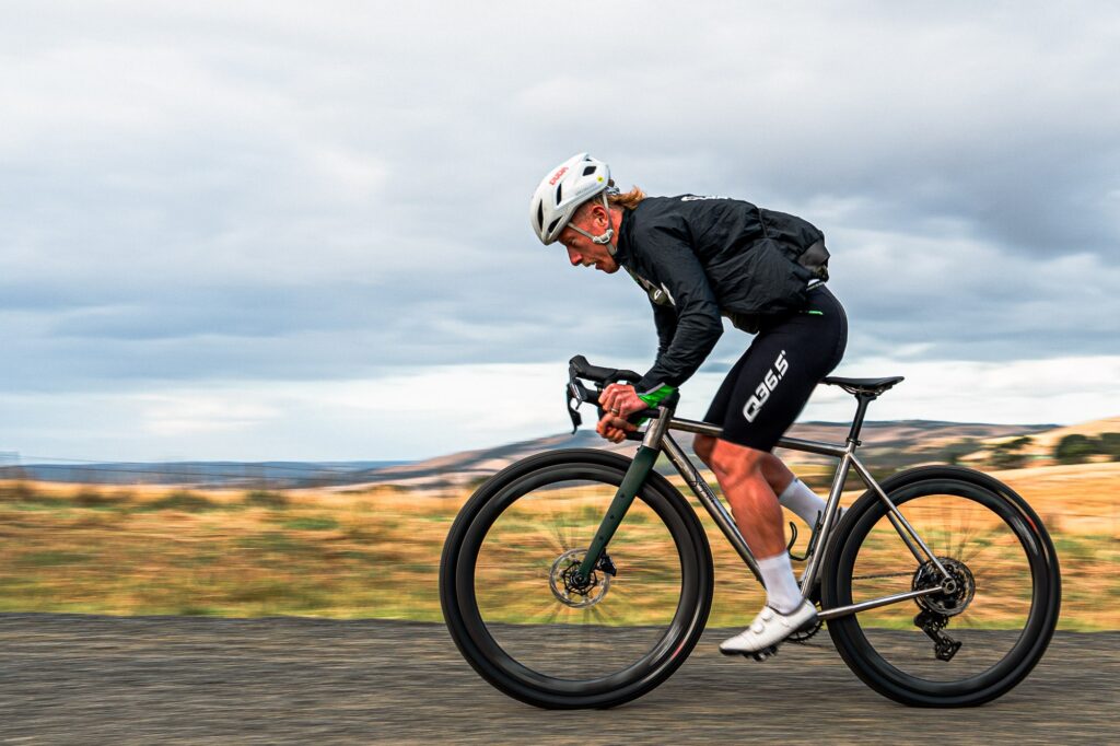 Rider on a titanium Simpatico N1 road bike with deep carbon wheels on a sealed country road