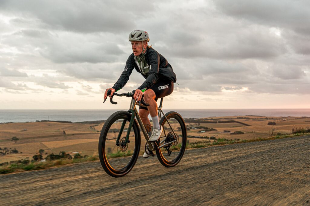 Rider on a Simpatico N1 in its gravel setup on a gravel road above farmland